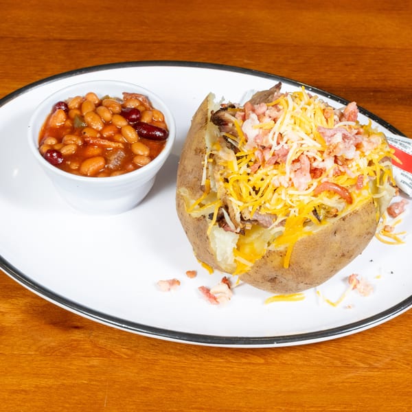 Loaded baked potato with cheese, bacon, and meat, served with a side of baked beans.