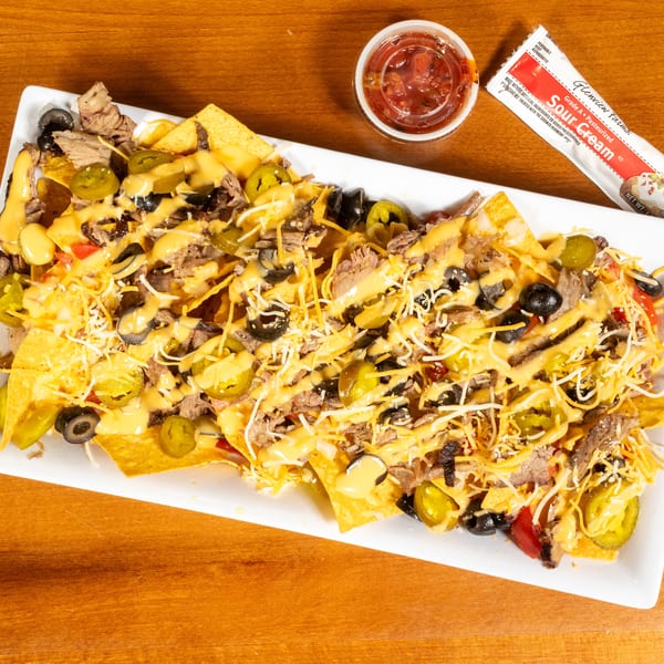 A large platter of loaded nachos with beef, cheese sauce, jalapeños, olives, and shredded cheese.