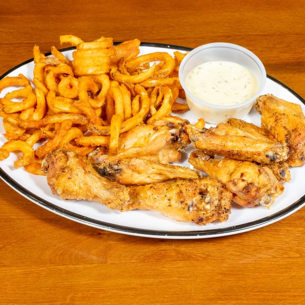 A white plate with crispy curly fries, seasoned chicken wings, and a side of ranch dressing.