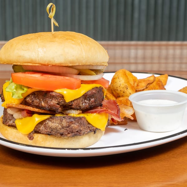 Double cheeseburger with bacon, lettuce, tomato, onion, and pickles, served with potato wedges and dip.