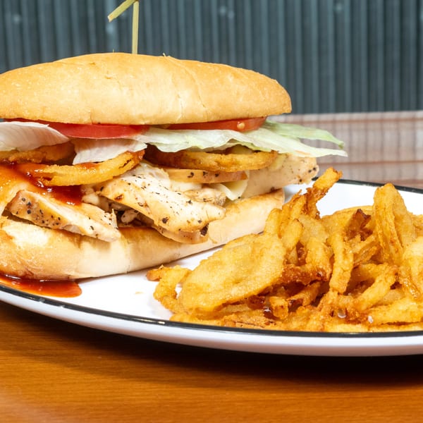 Chicken sandwich with BBQ sauce, melted cheese, lettuce, tomato, and crispy onion rings, served with fries.