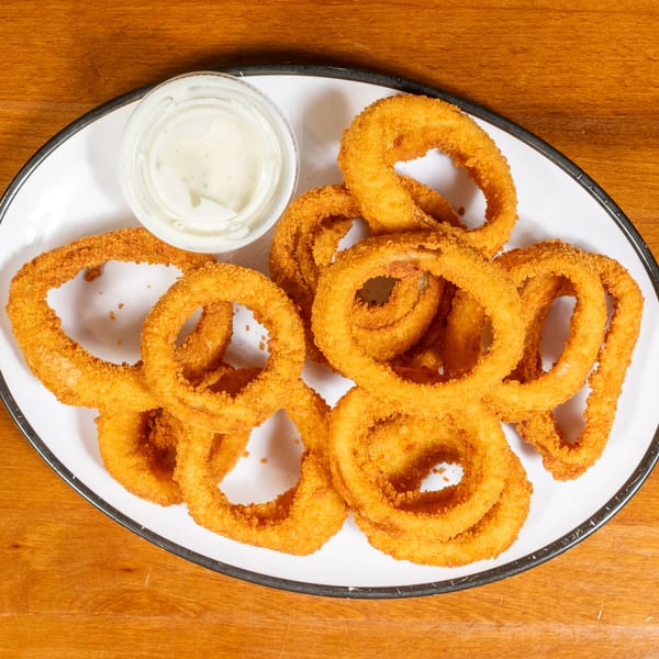 A white oval plate filled with golden-brown onion rings and a small cup of dipping sauce.