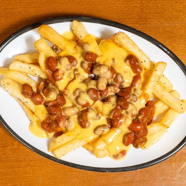 A white oval plate filled with golden french fries, topped with chili and melted cheese sauce.