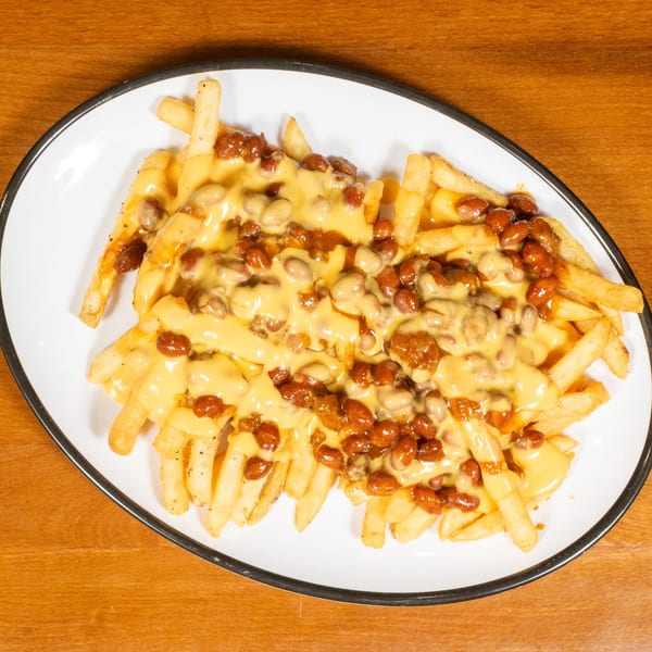 Chili cheese fries on a white oval plate with a black rim, on a wooden table.