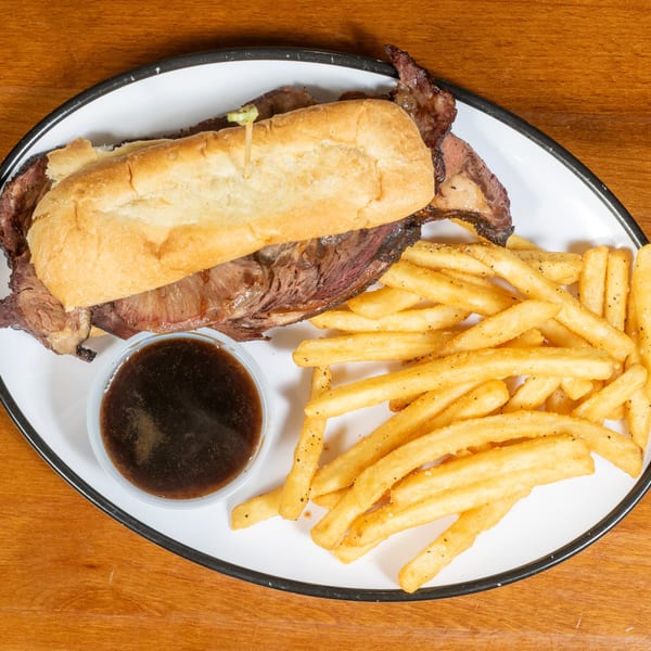 Brisket sandwich on a white plate with a side of french fries and a small cup of au jus.