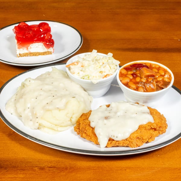 A fried chicken steak with gravy, mashed potatoes, coleslaw, baked beans, and cherry cheesecake.
