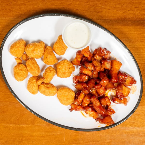 A white oval plate with crispy tater tots, saucy boneless wings, and a side of ranch dressing.