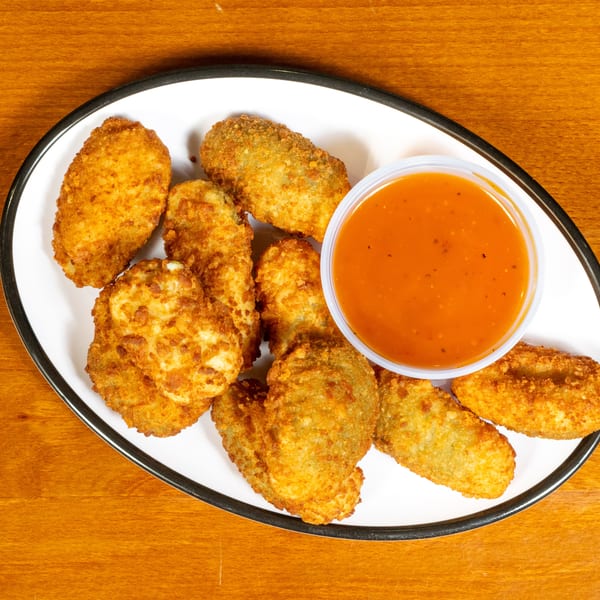 A white oval plate with crispy fried jalapeño poppers and a side of orange dipping sauce.
